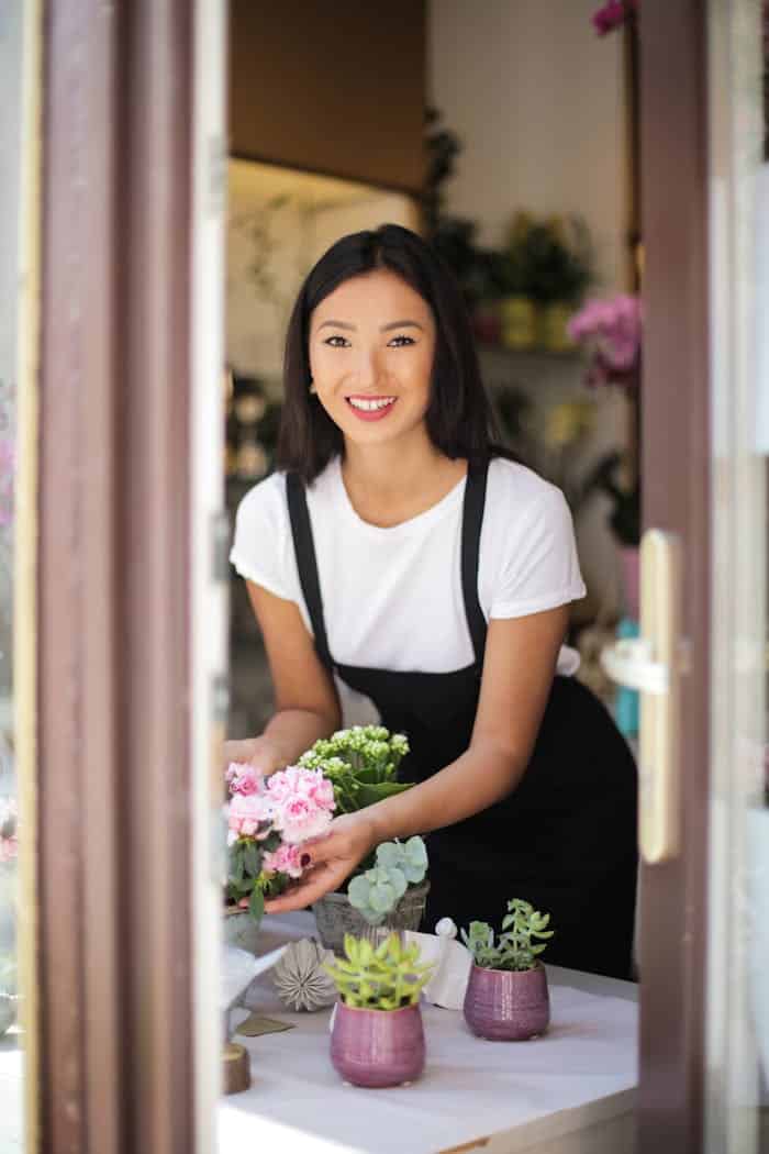 our-services-3 A cheerful florist arranges fresh flowers on a table inside a quaint flower shop.