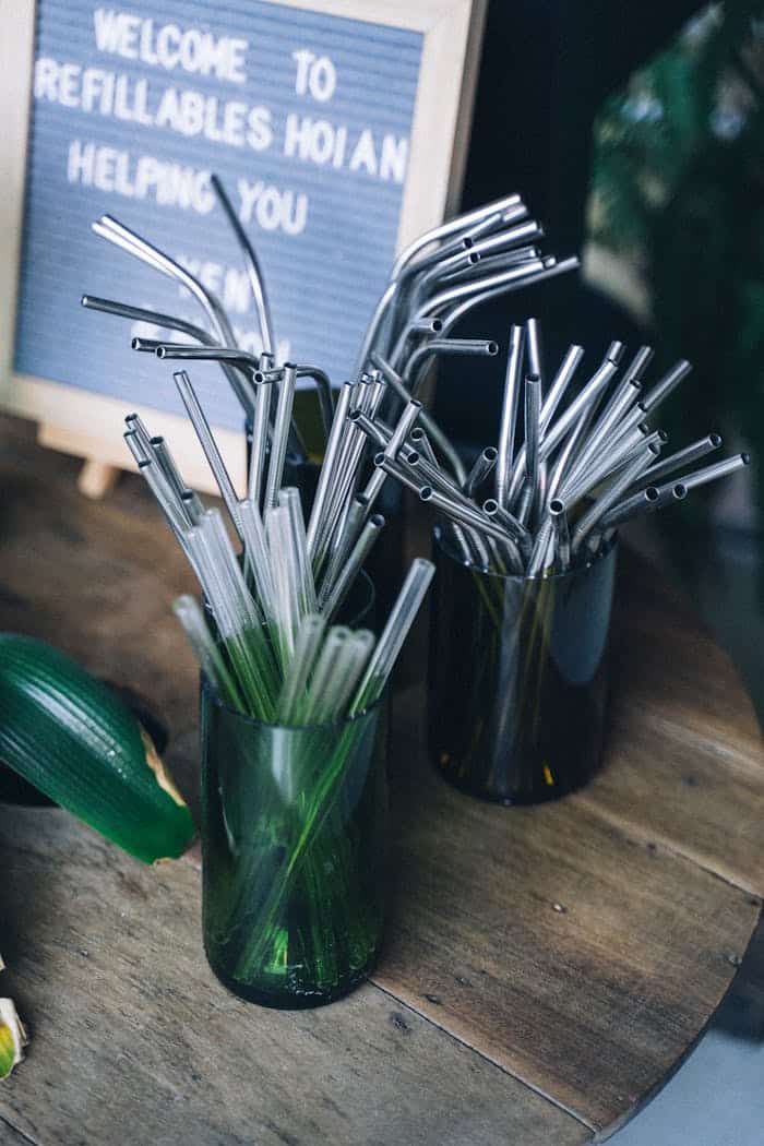 our-services-2 A display of reusable metal and glass straws in green vases, promoting sustainable living.